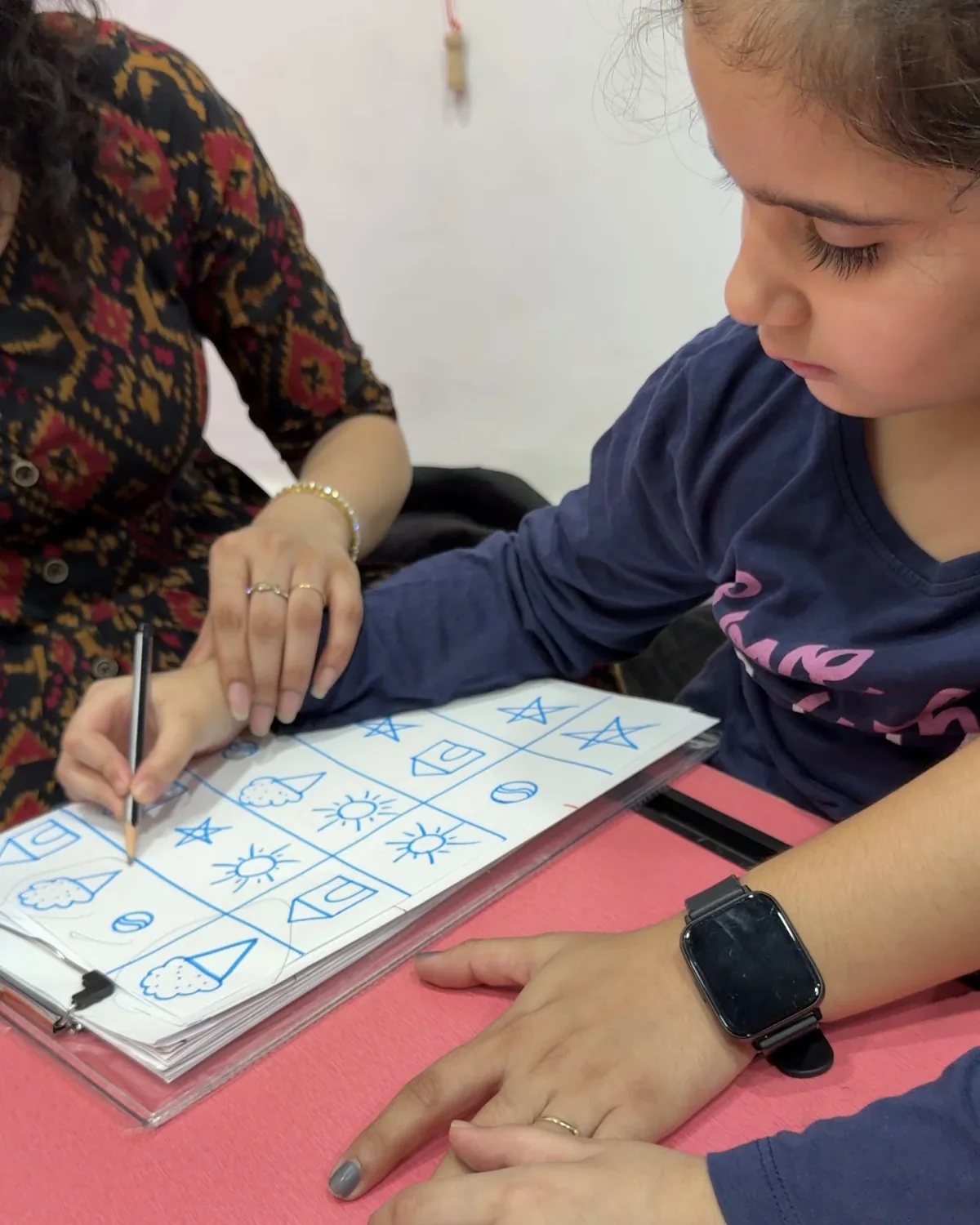 A girl practising shapes and writing with her educator